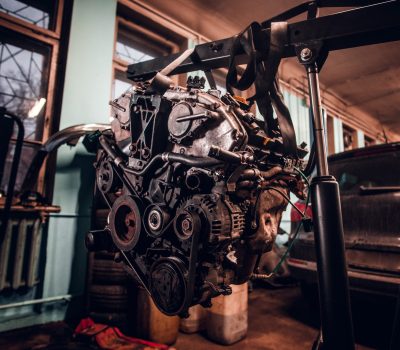Car engine with hinged equipment suspended on a hydraulic hoist in the workshop